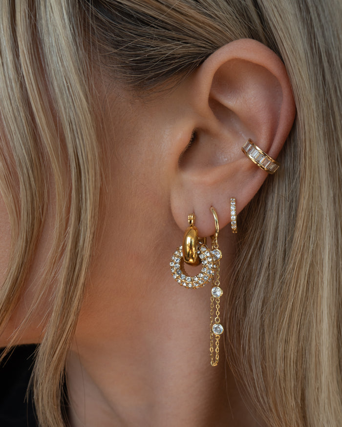 Close-up of an ear with multiple gold and crystal earrings