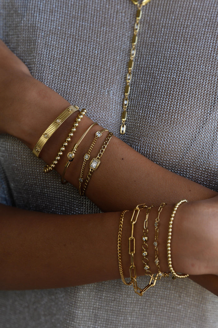 Close up of two wrists with gold bracelets on a dark background