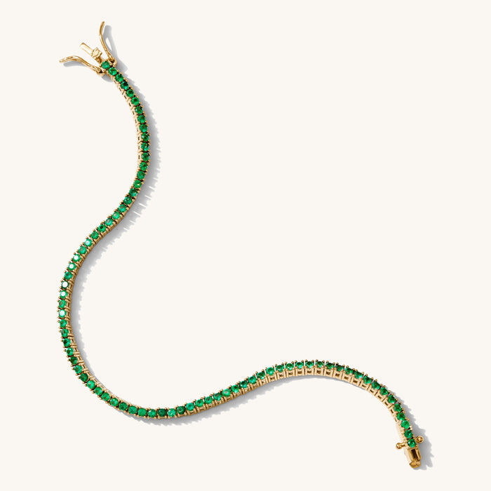 Close up of a tennis bracelet with green stones on a white background