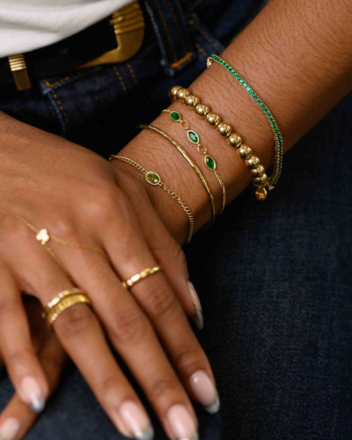 Close up of a person wearing gold and green bracelets, a white tank top, and blue jeans