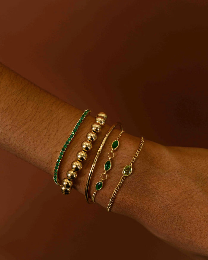 Close up of assorted gold and green bracelets on a brown background