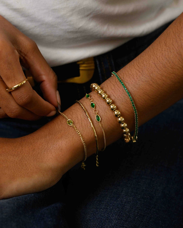 Close up of a person wearing gold and green bracelets, a white tank top, and blue jeans