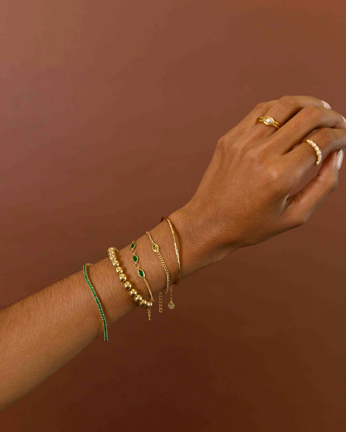 A hand with gold and stone bracelets and rings on a brown background