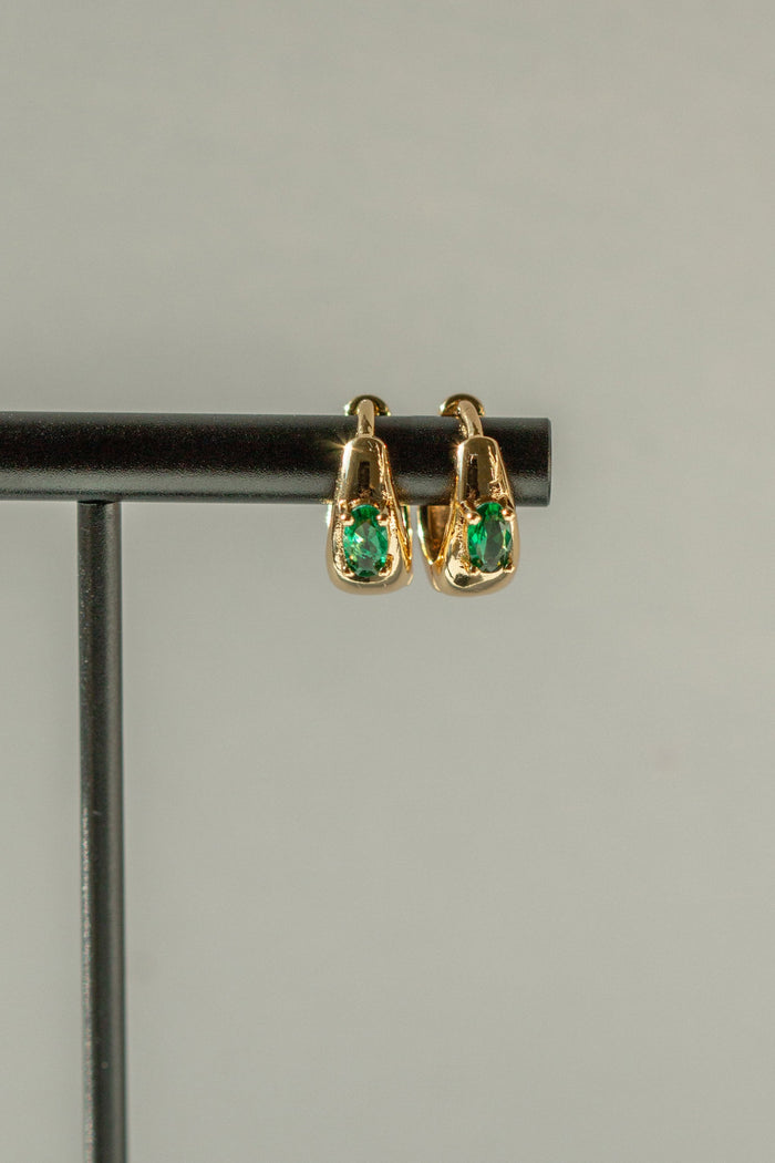 Gold earrings with green stones on a black bar