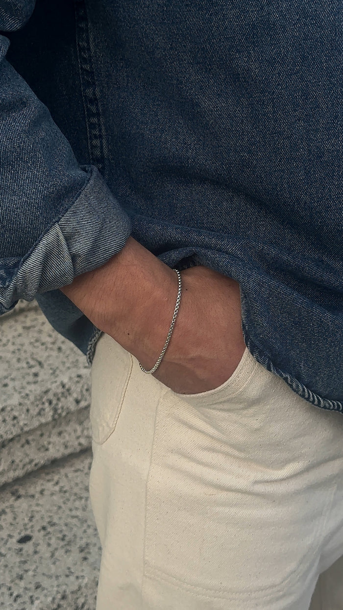 A man wearing a blue shirt, white pants, and a silver bracelet