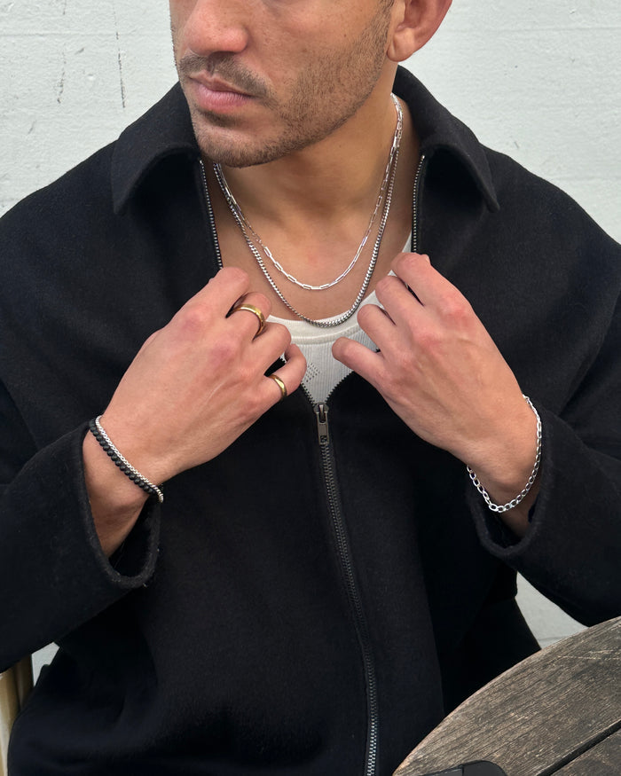 A man wearing a black shirt, black pants, white sneakers, and assorted silver jewelry