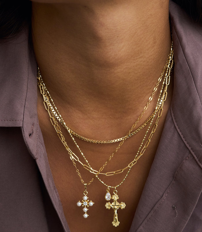 The gold Ernestina necklace pairing an ornate cross with a bezel-set pear stone