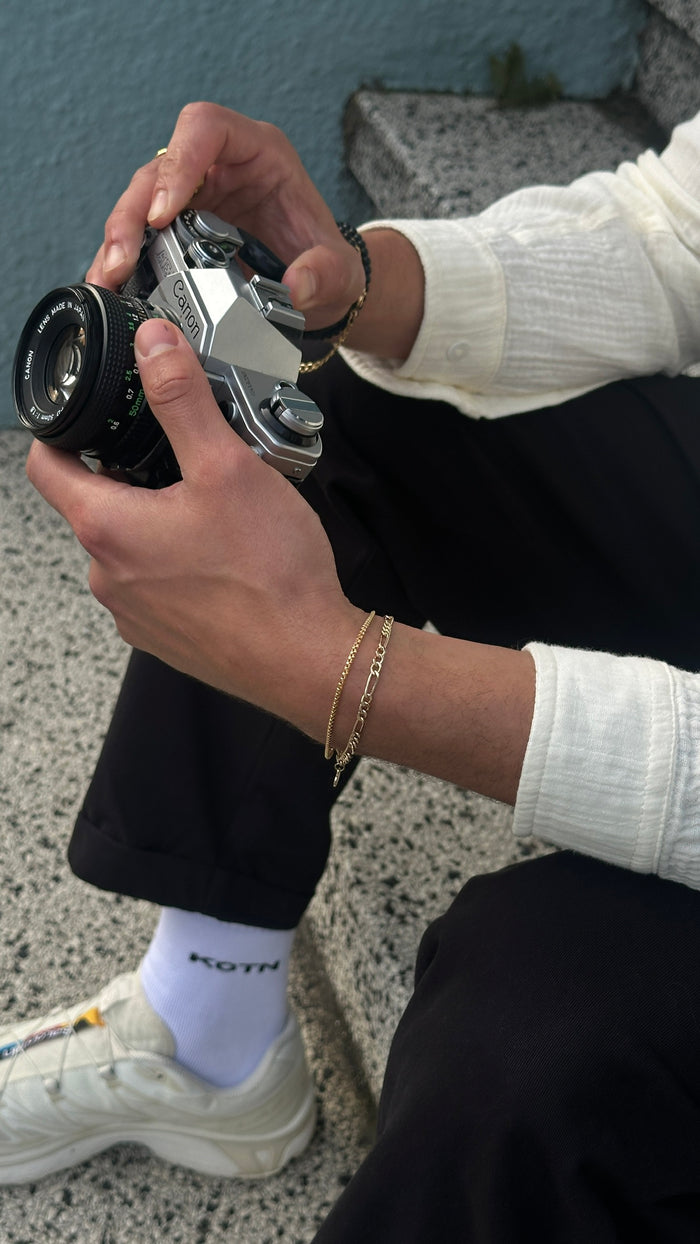 A person siting on a staircase holding a camera, wearing black and white clothes and gold jewelry