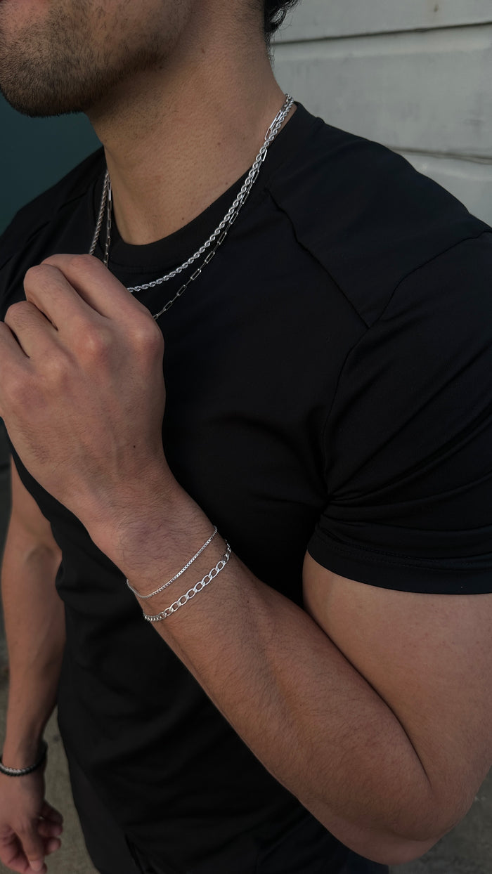 Close up of a man wearing a black t-shirt and various silver jewelry