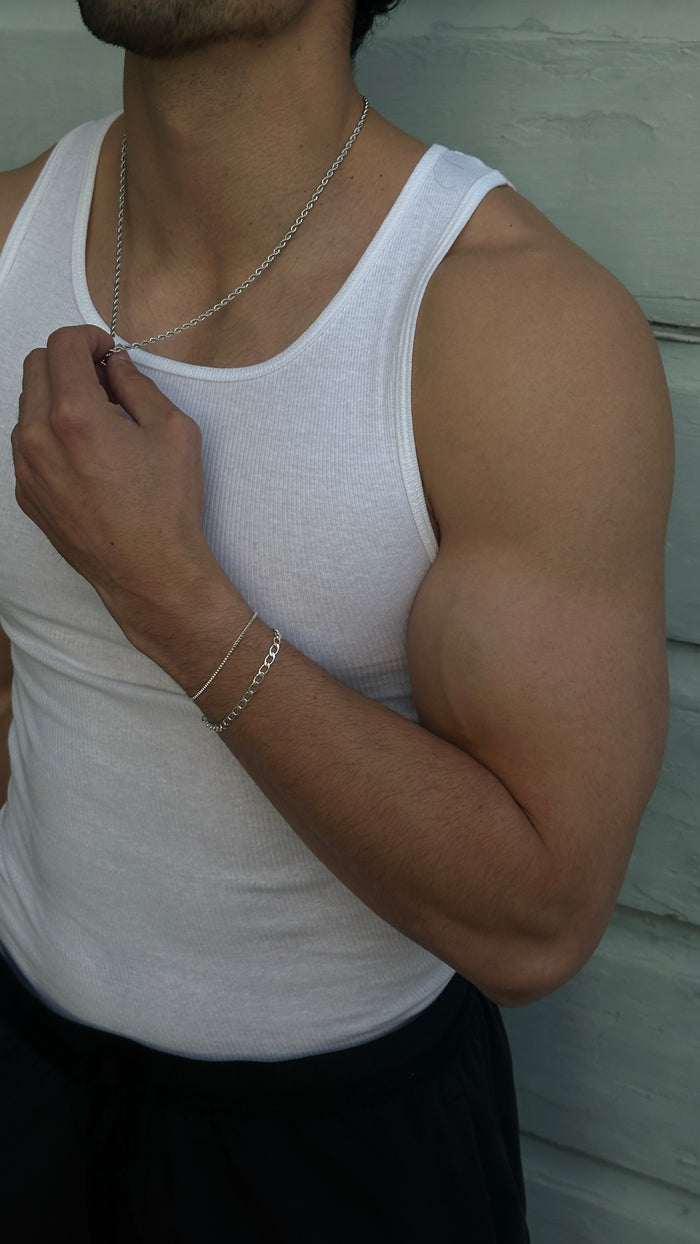 Close up of a man wearing a white tank top and various silver jewelry