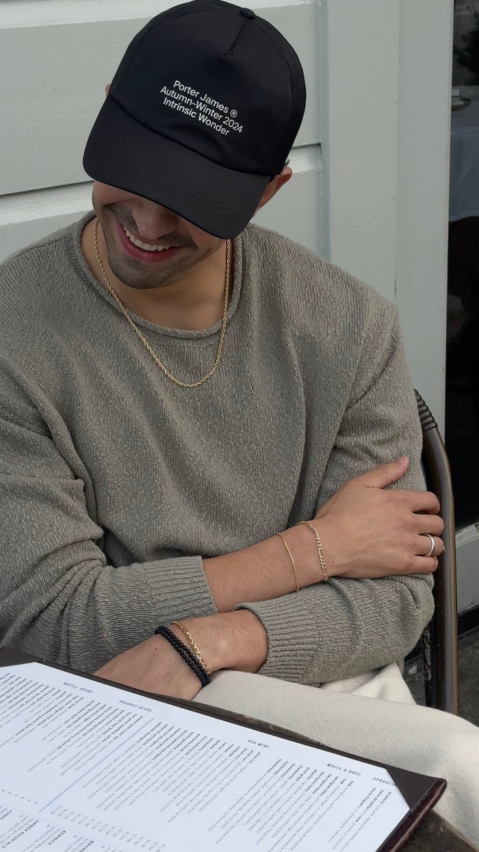 A man wearing a baseball cap, grey sweater, and assorted silver bracelets