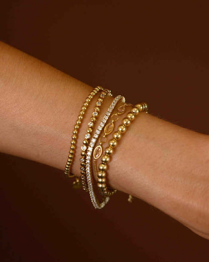 Close up of a wrist with assorted gold and stone bracelets on a brown background