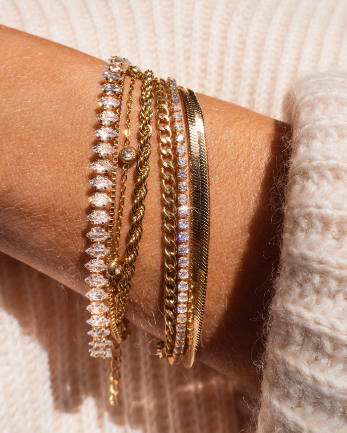 Close up of a wrist with gold and stone bracelets in a cream sweater