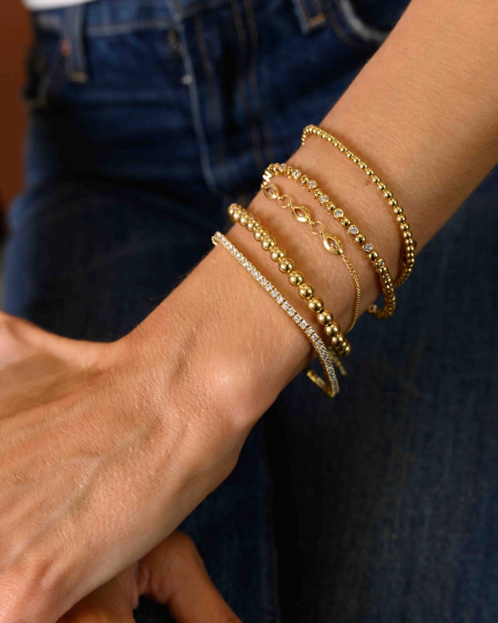 Close up of a person wearing blue jeans and gold bracelets on a brown background