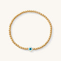 Close up of a gold bead bracelet with an evil eye bead