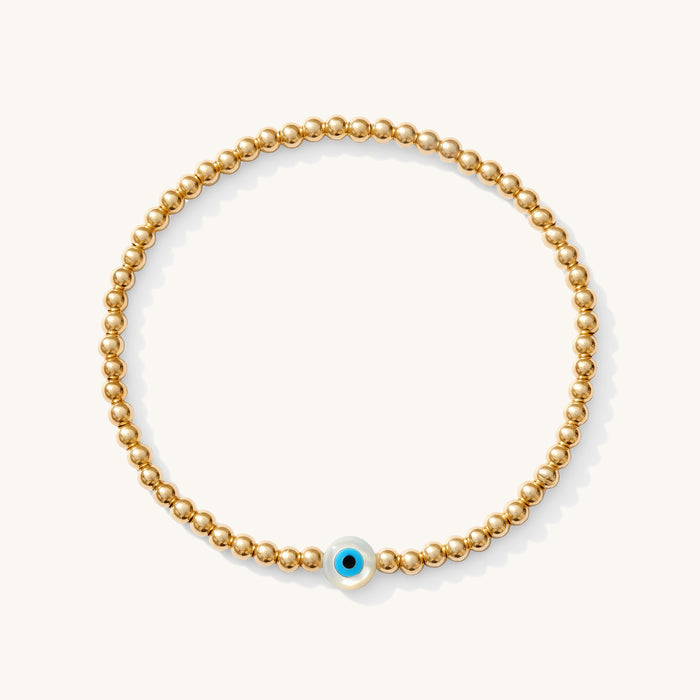 Close up of a gold bead bracelet with an evil eye bead
