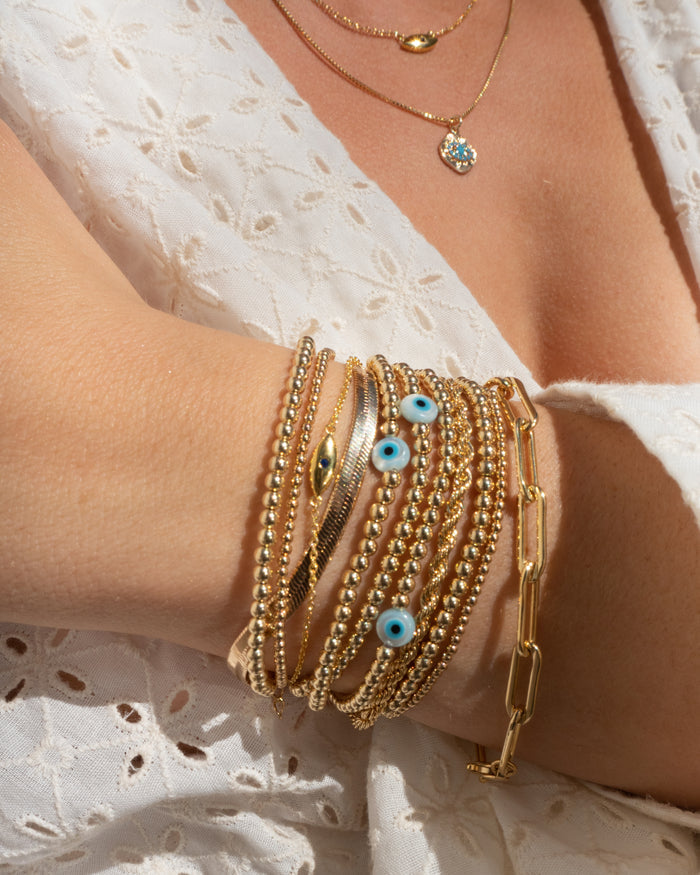 Close up of a person wearing a white blouse and gold jewelry with evil eye accents