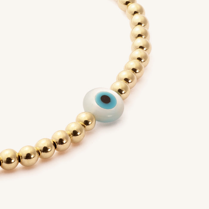 Close up of a gold bead bracelet with an evil eye bead