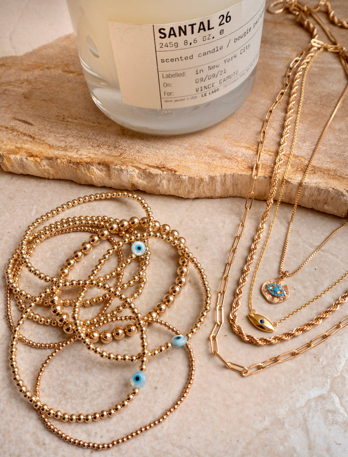 A wooden board with a candle and assorted gold jewelry with evil eye accents