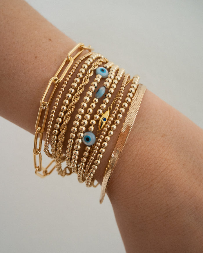 Close up of a wrist with assorted gold bracelets with evil eye accents on a grey background