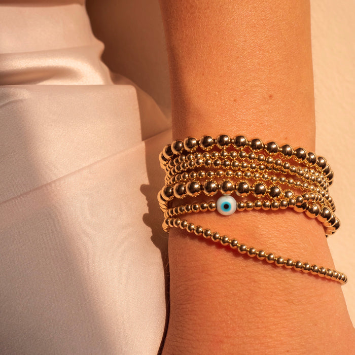 Close up of a wrist with assorted gold bracelets with evil eye accents on a white background
