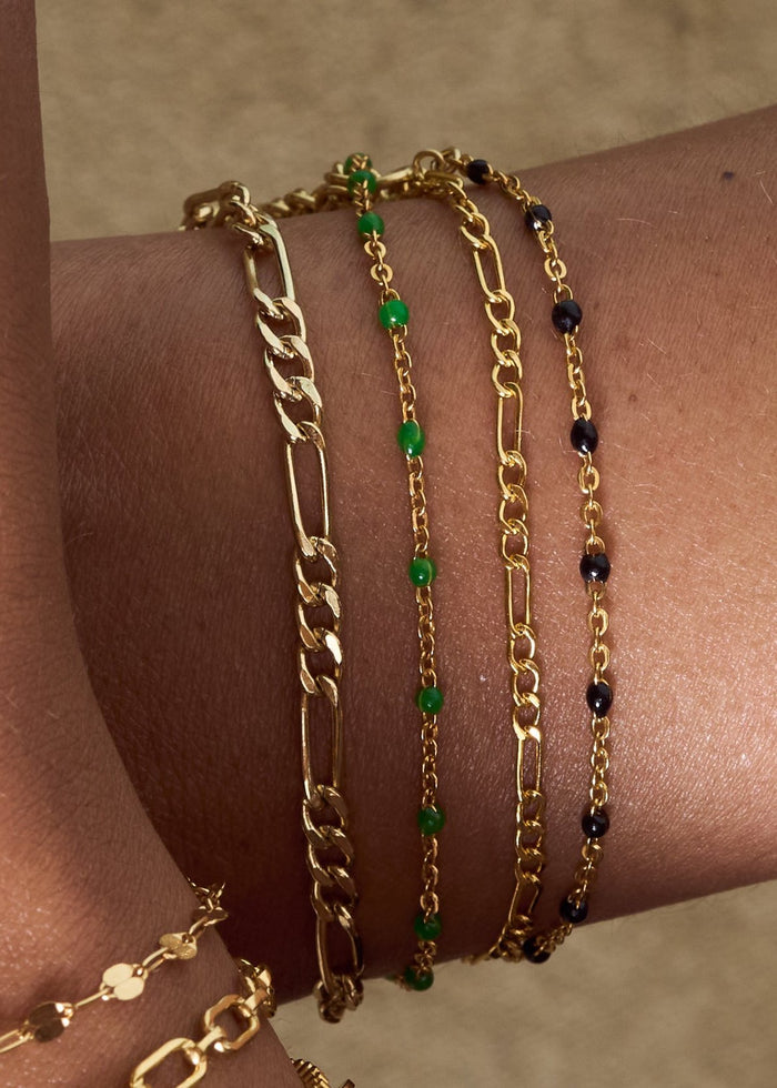 Close up of two wrists with dainty gold chain bracelets on a tan background