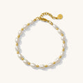 Close up of a gold bracelet with pearl beads on a white background