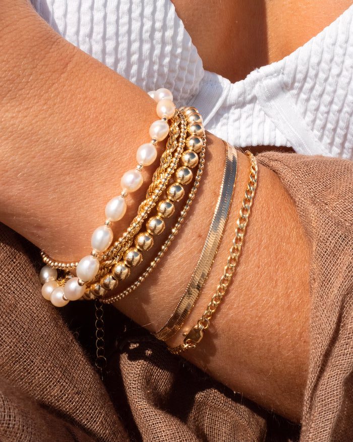 Close up of a person wearing a white bikini top and gold bracelets