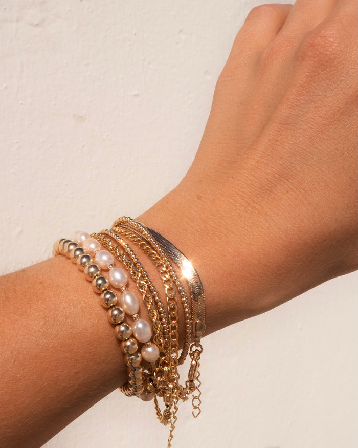 Close up of a wrist with gold and pearl bracelets on a white background