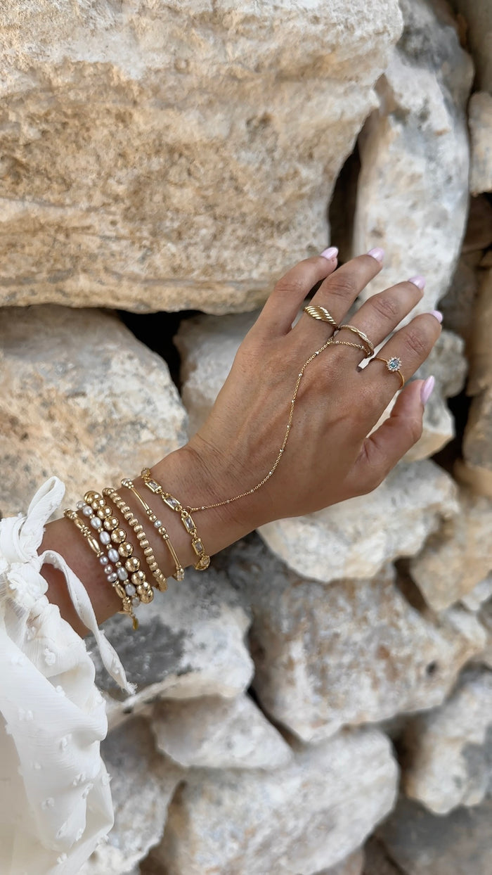 A hand with gold rings and bracelets on a backdrop of rocks