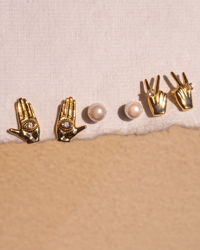 Three pairs of gold and pearl stud earrings on a neutral surface