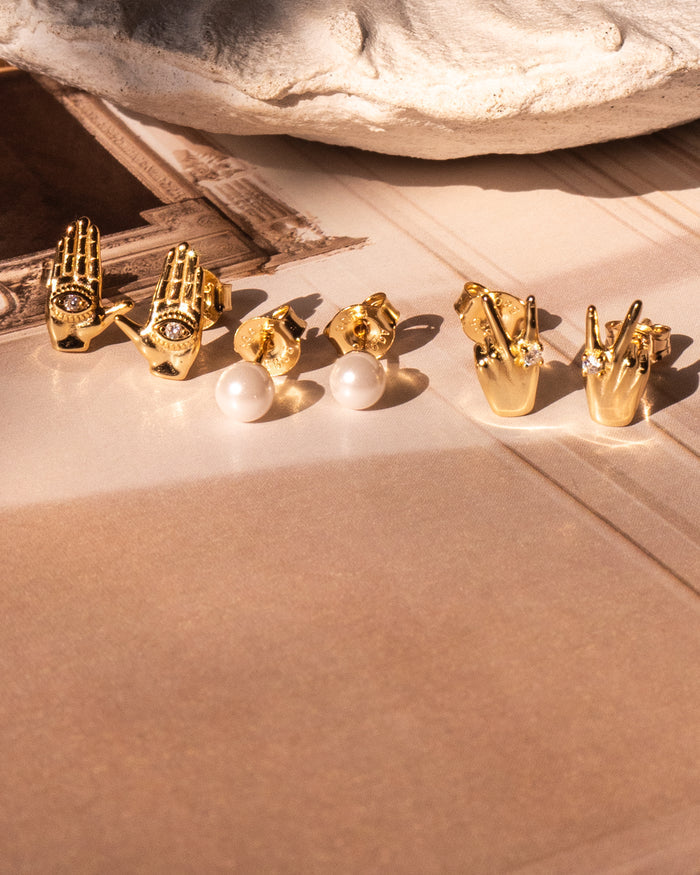 Three pairs of gold stud earrings on a neutral surface