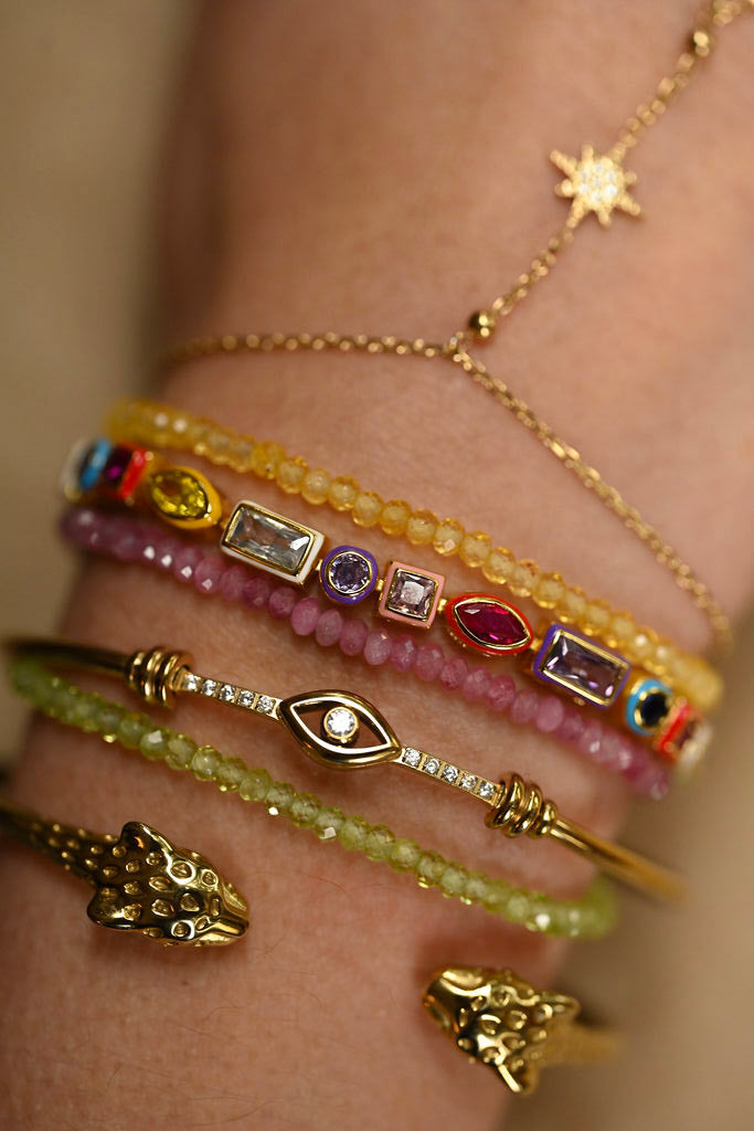 Close-up of a hand wearing multiple gold and gemstone bracelets on a neutral background