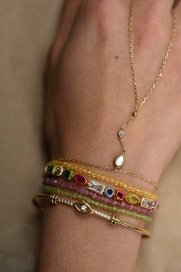 Close-up of a person's wrist wearing multiple gold bracelets with gemstones on a neutral background