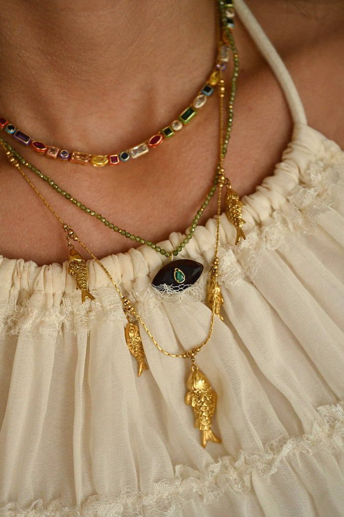 Close-up of a person wearing multiple necklaces with intricate designs on a beige background.