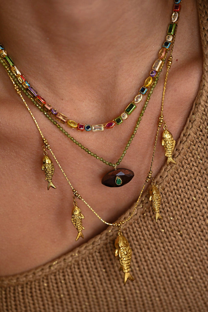 Close-up of a person wearing a gold necklace with fish charms and colorful beads.