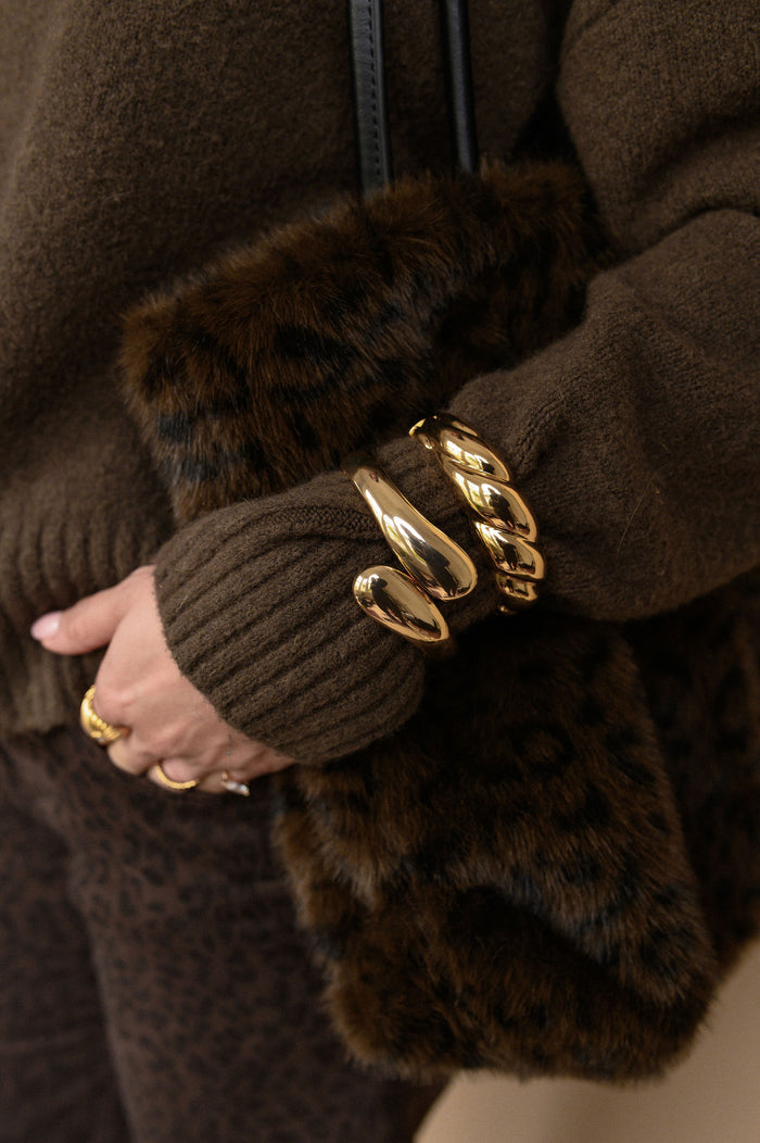 Close-up of a person wearing a brown sweater and fur bag with gold bracelets.