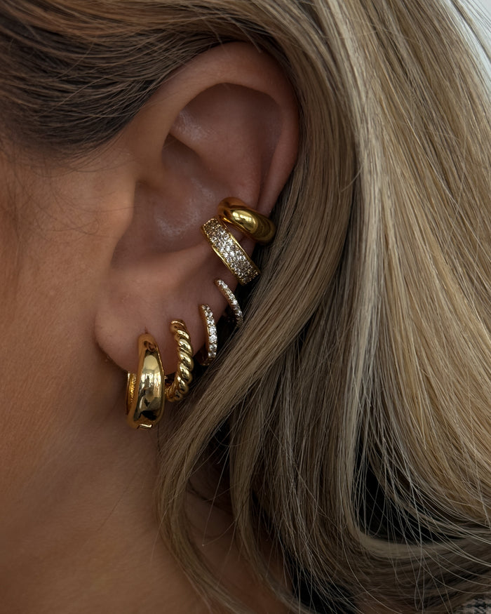 Close-up of an ear with multiple gold and crystal earrings
