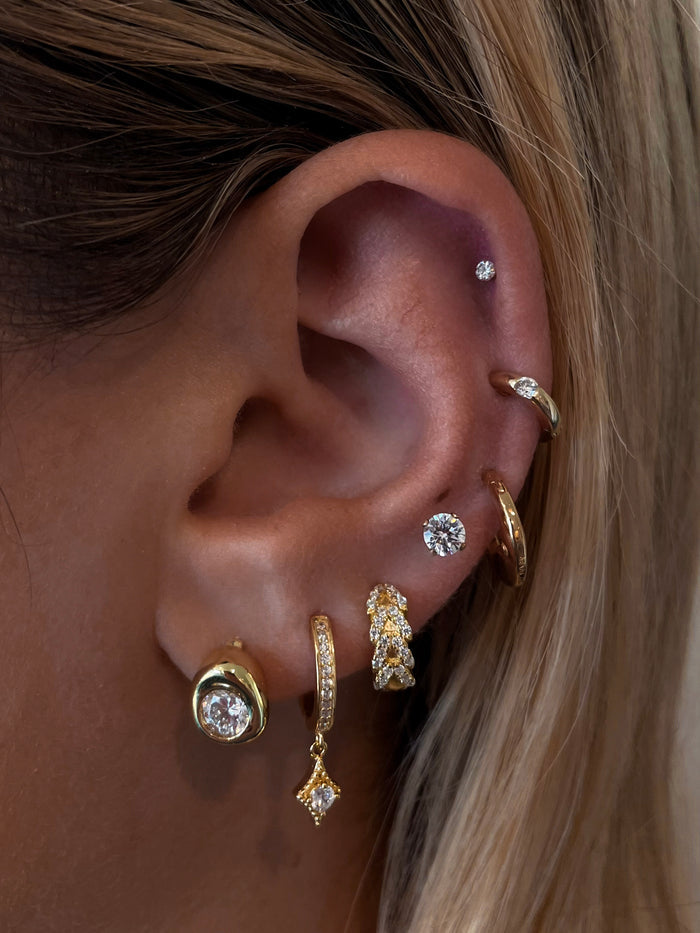 Close-up of an ear with multiple gold and crystal earrings
