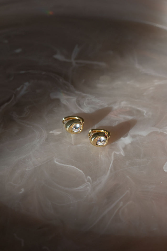 Gold earrings on a cream marble surface