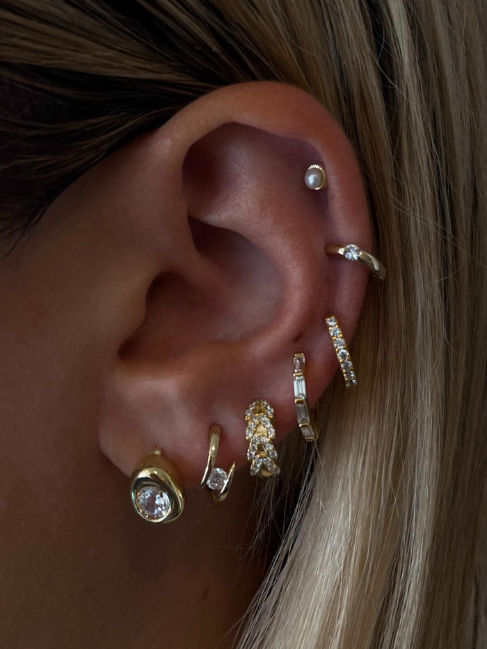 Close-up of an ear with multiple gold and crystal earrings