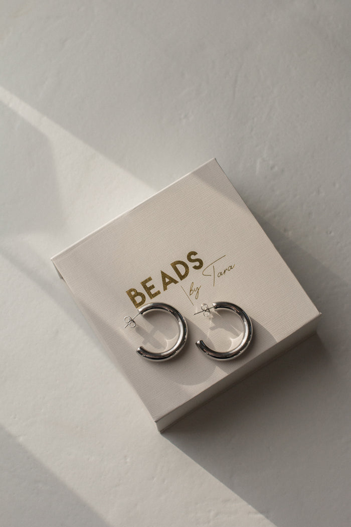 A pair of silver hoop earrings on a jewelry gift box that says "Beads by Tara"