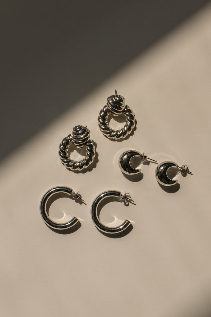 Three pairs of silver accent earrings on a netural surface