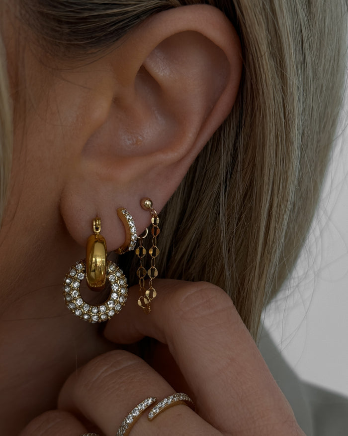 Close-up of an ear with multiple gold and crystal earrings