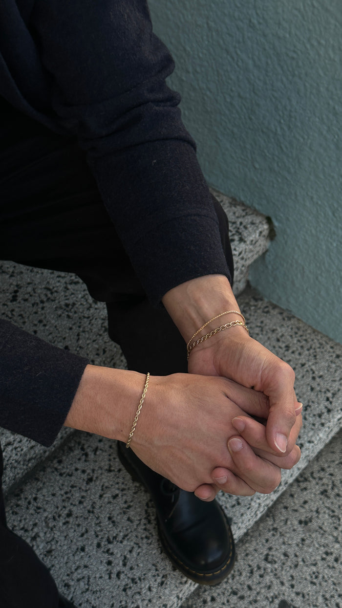 A person sitting on a staircase wearing black clothing and gold bracelets
