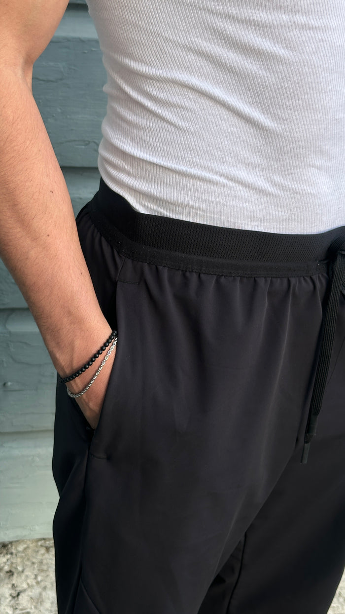 Close up of a man wearing a white tank top, black pants, and various bracelets