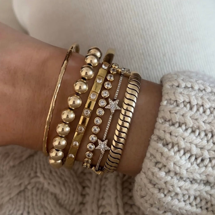 Close up of a wrist with a cream sweater and assorted gold and stone bracelets