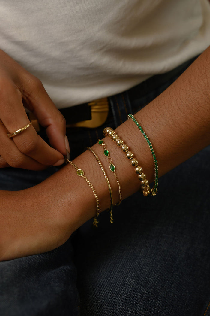 Close up of person wearing a white shirt, blue jeans, and assorted gold and green bracelets