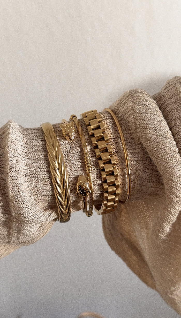 A textured sweater sleeve wearing multiple gold bracelets