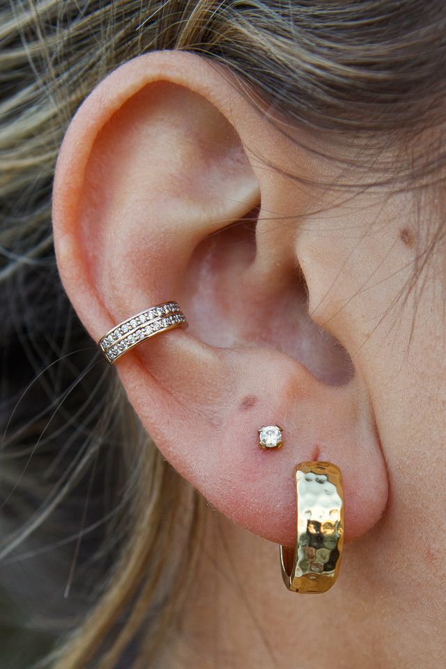 Close-up of an ear with multiple gold and crystal earrings